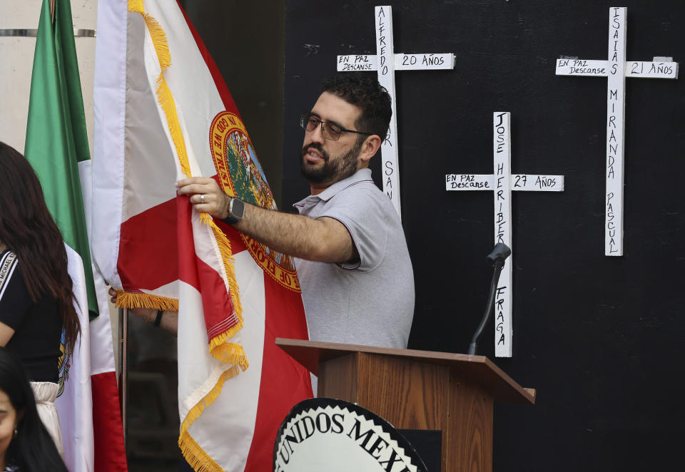 A flag is unfurled in front of the Mexican Consulate in Orlando, Fla., Tuesday, May 21, 2024, for a vigil honoring the eight Mexican farmworkers who were killed in a bus crash last week in Marion County. (Stephen M. Dowell/Orlando Sentinel via AP)