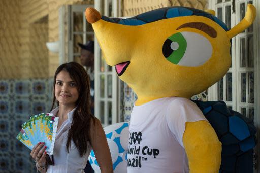Una aficionada posa con sus boletos para el Mundial de Brasil junto a la mascota del evento, el 18 de abril de 2014, en Rio de Janeiro (AFP | YASUYOSHI CHIBA)
