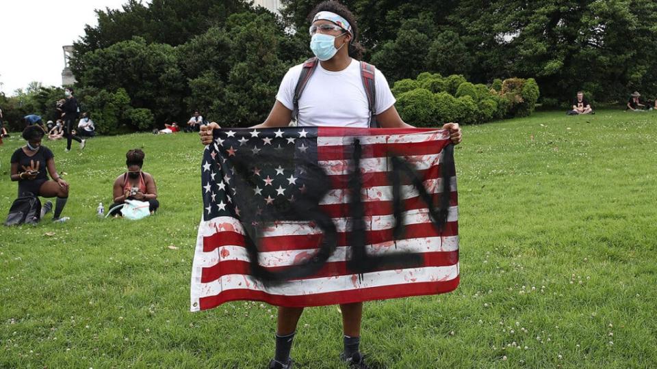 A demonstrator standing at the Lincoln Memorial holds an American flag with “BLM” painted on it during a protest against police brutality and racism on June 6, 2020 in Washington, DC. (Photo by Win McNamee/Getty Images)