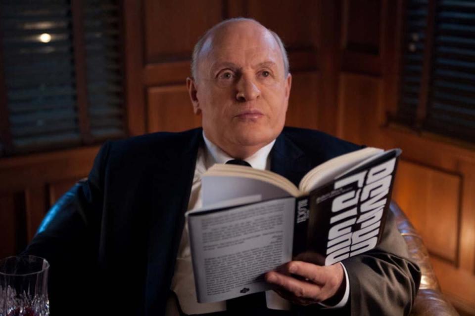 Anthony Hopkins as Alfred Hitchcock in a black suit hoding a book titled Psycho