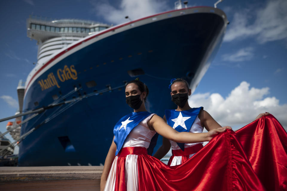 Ivanelis Jimenez, front, and Veronica Barreto pose for the camera wearing Puerto Rican flag dresses as they welcome passengers exiting Carnival's Mardi Gras cruise ship, docked in the bay of San Juan, Puerto Rico, Tuesday, Aug. 3, 2021, marking the first time a cruise ship visits the U.S. territory since the COVID-19 pandemic began. (AP Photo/Carlos Giusti)