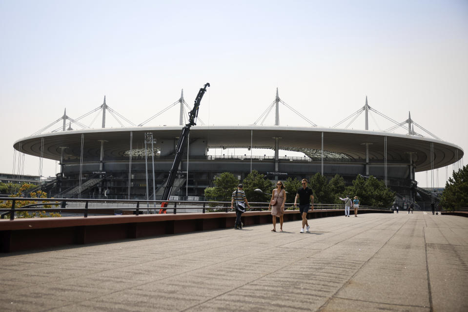 Varias personas caminan cerca del Stade de France, el lunes 10 de julio de 2023, en Saint-Denis. El estadio será la sede del atletismo y el rugby de siete en los Juegos Olímpicos de París de 2024. (AP Foto/Thomas Padilla)