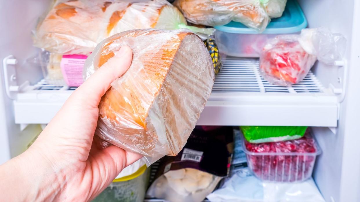 a hand putting a package of brown bread in reserve on a shelf of a home freezer, long life food storage concept