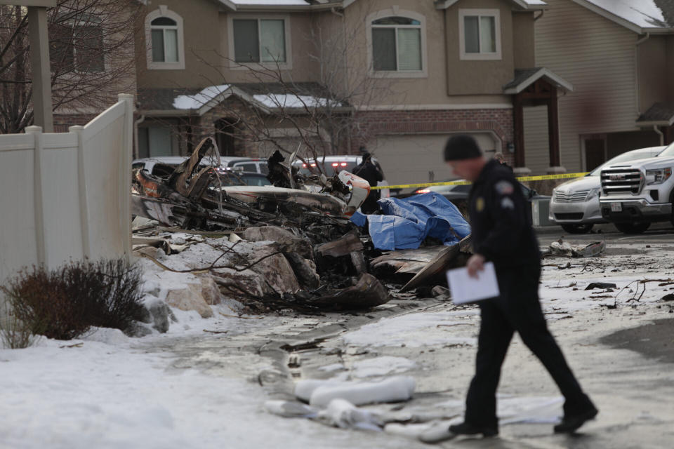 An investigator walks near the debris from a small private plane that crashed in a residential area Wednesday, Jan. 15, 2020, in Roy, Utah. The small plane crashed Wednesday, killing the pilot as the aircraft narrowly avoided hitting any townhomes, authorities said. (Ben Dorger/Standard-Examiner via AP)