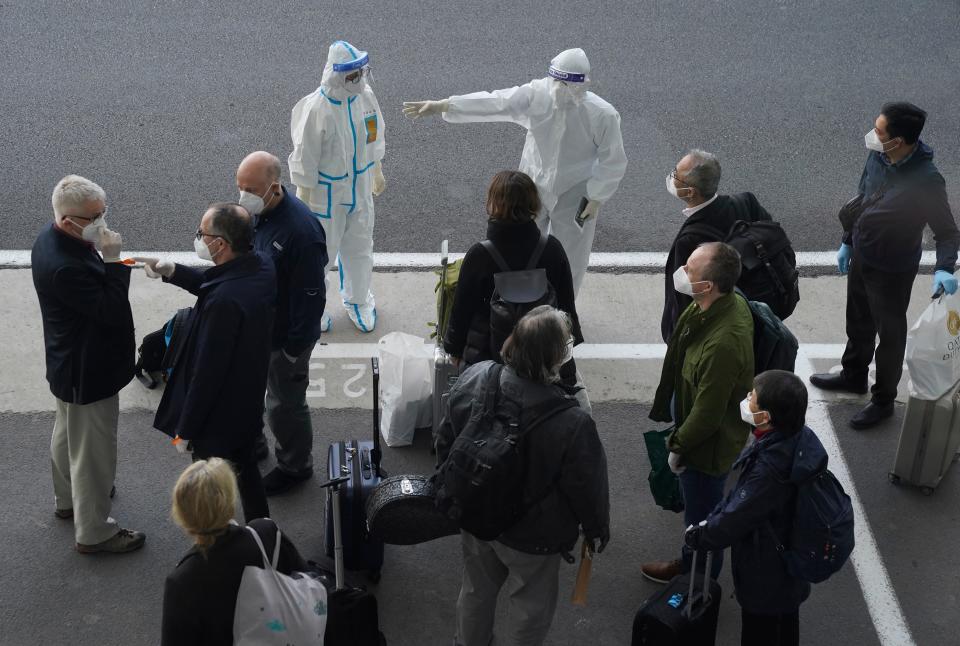 A worker in protective coverings directs members of the World Health Organization (WHO) team on their arrival at the airport in Wuhan in central China's Hubei province on Thursday, Jan. 14, 2021. A global team of researchers arrived Thursday in the Chinese city where the coronavirus pandemic was first detected to conduct a politically sensitive investigation into its origins amid uncertainty about whether Beijing might try to prevent embarrassing discoveries.