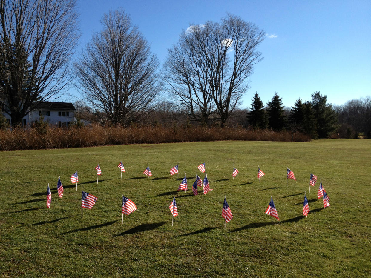 Twenty-six flags, one for each victim of the massacre at Sandy Hook, are displayed in a circle on a lawn.