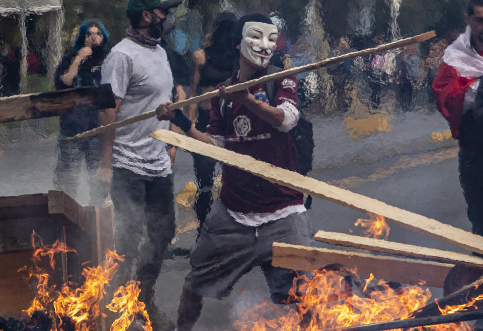 A demonstrator wearing a mask throws a plank of wood into a flaming barricade during a protests in Santiago, Chile, Saturday, Oct. 19, 2019. The protests started on Friday afternoon when high school students flooded subway stations, jumping turnstiles, dodging fares and vandalizing stations as part of protests against a fare hike, but by nightfall had extended throughout Santiago with students setting up barricades and fires at the entrances to subway stations, forcing President Sebastian Pinera to announce a state of emergency and deploy the armed forces into the streets. (Photo: Esteban Felix/AP)