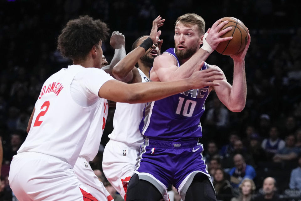 Sacramento Kings' Domantas Sabonis (10) protects the ball from Brooklyn Nets' Cameron Johnson (2) and Mikal Bridges during the first half of an NBA basketball game Thursday, March 16, 2023, in New York. (AP Photo/Frank Franklin II)