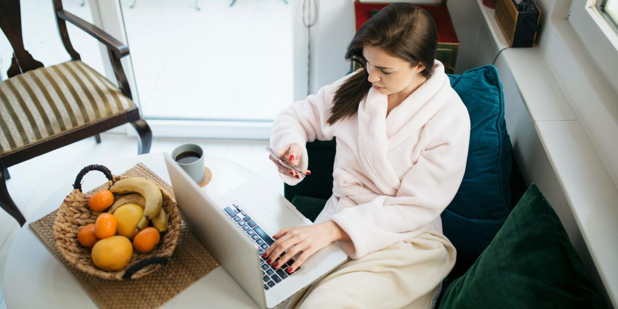 woman in robe working from laptop and phone