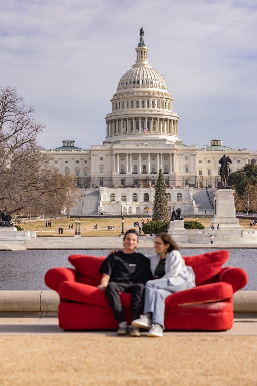 Adrian Delli Colli and Amy Hage sit on the red couch that is traveling the world as part of the Concept Project.