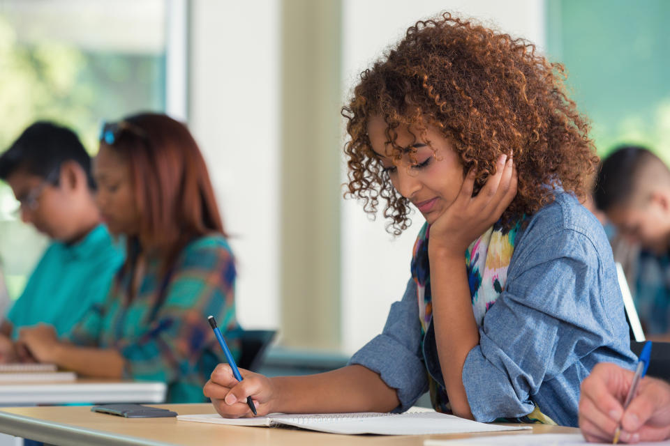 A group of focused students writing notes, one woman forefront with a thoughtful expression