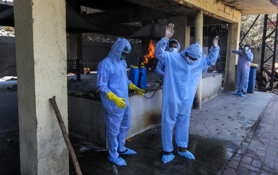 FILE- In this April 15, 2021 file photo, municipal workers in personal protective suits sanitize themselves after cremating a COVID-19 victim in Vasai, outskirts of Mumbai, India. India's health system is collapsing under the worst surge in coronavirus infections that it has seen so far. Medical oxygen is scarce. Intensive care units are full. Nearly all ventilators are in use, and the dead are piling up at crematoriums and graveyards. Such tragedies are familiar from surges in other parts of the world — but were largely unknown in India. (AP Photo/Rafiq Maqbool, File)