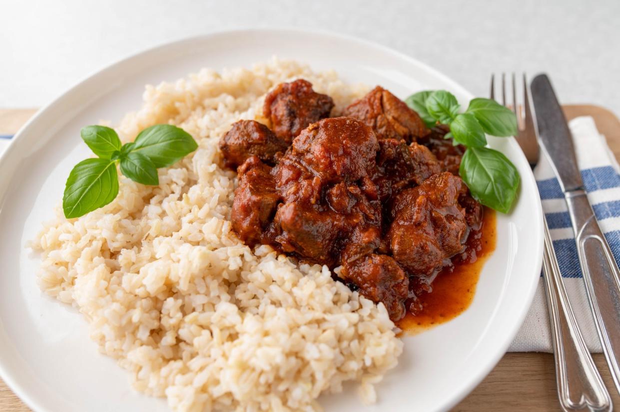 Delicious and healthy meal for dinner or lunch with braised low fat turkey meat and brown rice. Served ready to eat on a plate with knife and fork isolated on light background