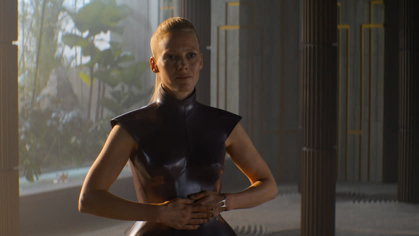 a young woman in a sleeveless black tunic stands in front of a window