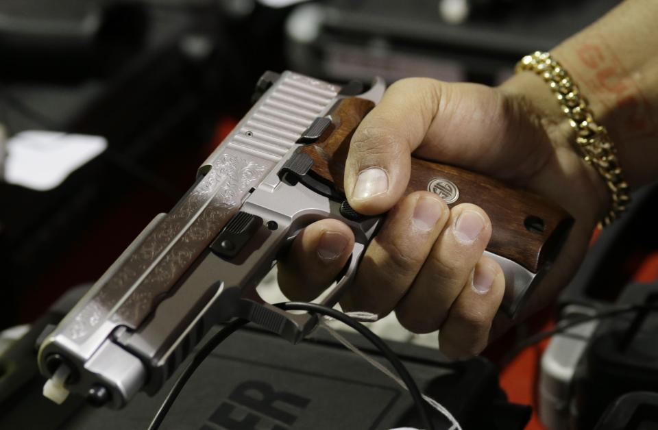 FILE - In this Jan. 9, 2016, file photo, a customer looks at a SIG Sauer hand gun at a gun show held by Florida Gun Shows in Miami.  The vast majority of mass shooters have acquired their firearms legally with nothing in their background that would have prohibited them from possessing a gun. But there have been examples of lapses in the background check system that allowed guns to end up in the wrong hands. Very few states also have a mechanism to seize firearms from someone who is not legally allowed to possess one.