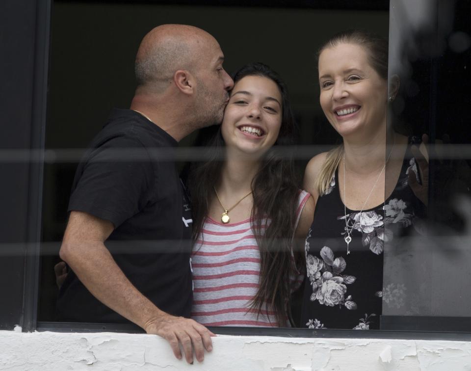 FILE - In this Sept. 20, 2014, file photo, appearing before journalists, Ivan Simonovis, former Caracas police chief, left, kisses his daughter Ivana, center, as his wife Bony smiles, while standing on the balcony of their Caracas, Venezuela, home where he spent nearly five years under house arrest. In Simonovis' first interview since escaping to the U.S. in June 2019, he shares details of his movie-like breakout. (AP Photo/Fernando Llano, File)