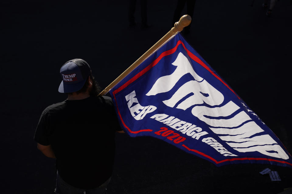 A supporter of President Donald Trump carries a Trump flag before a news conference by the Trump campaign in front of the Clark County Election Department, Thursday, Nov. 5, 2020, in Las Vegas. (AP Photo/John Locher)