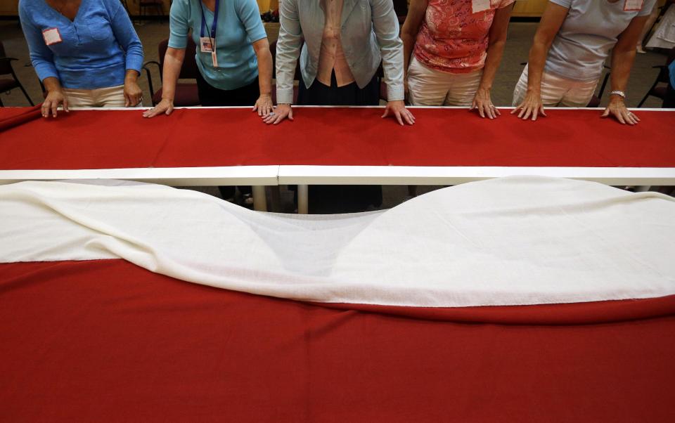 In this July 22, 2013 picture, volunteers smooth out sections of a replica of the star-spangled banner before they are sewn together in Baltimore. It was 200 years ago this summer that a Baltimore flag-maker stitched the flag that inspired America’s national anthem. Now, hundreds of people are helping to recreate the star-spangled banner. The project began July 4 in Baltimore, and it is expected to take volunteers six weeks to hand sew the estimated 150,000 stitches in the famous flag. When finished, it will be about a quarter of the size of a basketball court. (AP Photo/Patrick Semansky)