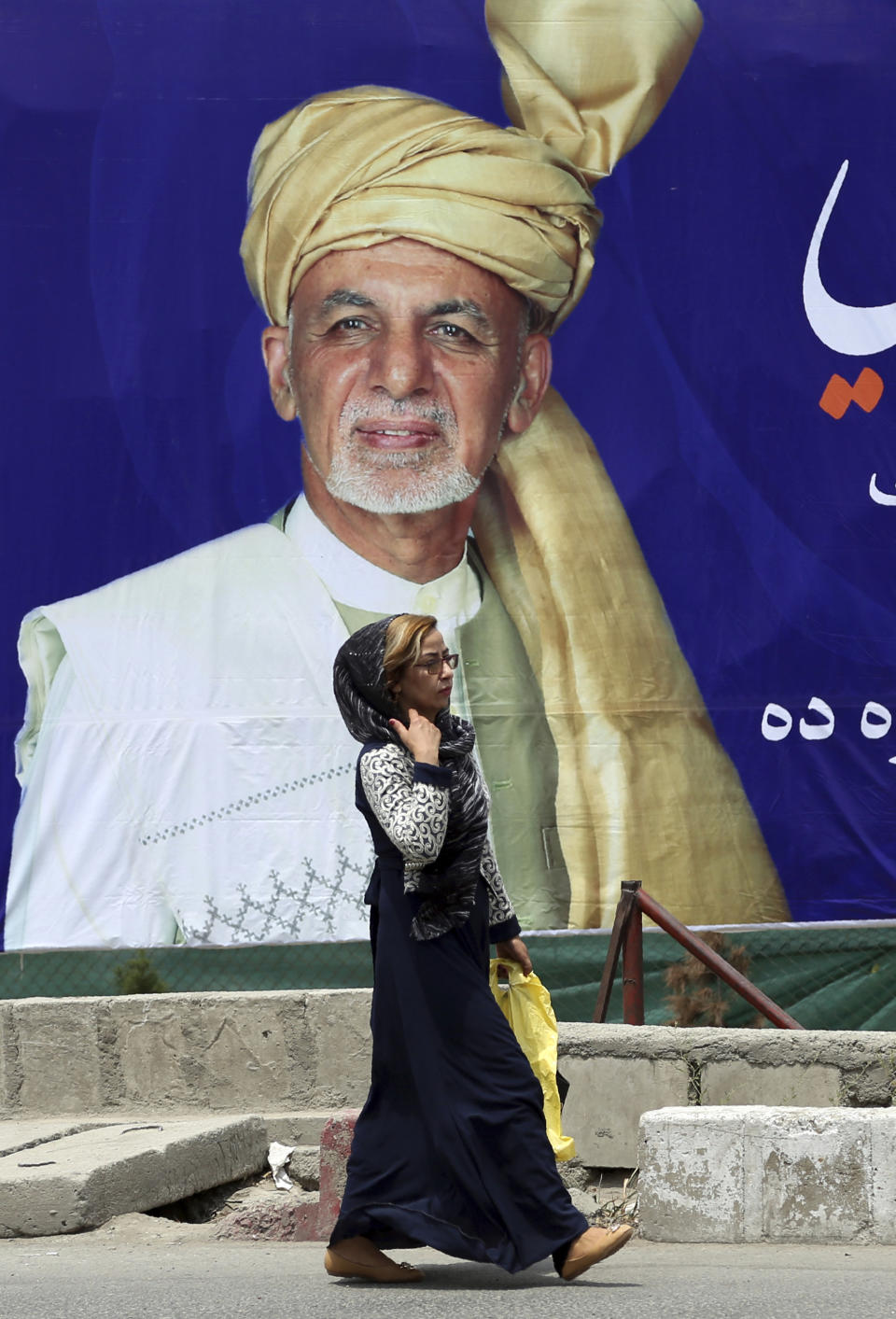 An Afghan woman walks past an election poster of presidential candidate Ashraf Ghani during the first day of campaigning in Kabul, Afghanistan, Sunday, July 28, 2019. Sunday marked the first day of campaigning for presidential elections scheduled for Sept. 28. President Ghani is seeking a second term on promises of ending the 18-year war but has been largely sidelined over the past year as the U.S. has negotiated directly with the Taliban. (AP Photo/Rahmat Gul)