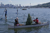 People paddle a canoe with a Christmas tree held up by hockey sticks as they float on Lake Union with the Space Needle in the background, Wednesday, July 21, 2021, in Seattle near the park where the Seattle Kraken NHL hockey expansion draft event was taking place. (AP Photo/Ted S. Warren)