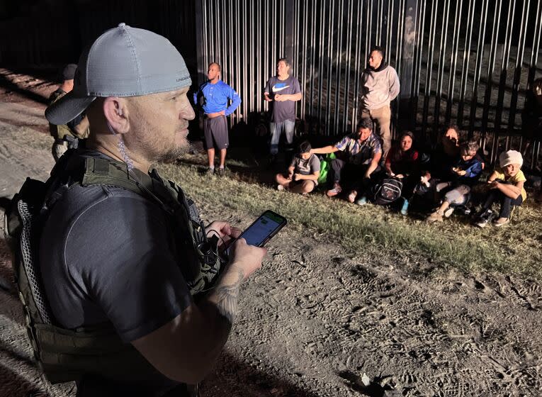 EAGLE PASS TEXAS APRIL 12, 2022 - Samuel Hall, 40, North Texas-based founder of the Patriots for America militia, surveys a group of migrants stopped by U.S. Customs and Border Protection agents after crossing the Rio Grande in Eagle Pass, Texas, last month. (Molly Hennessy-Fiske / Los Angeles Times)