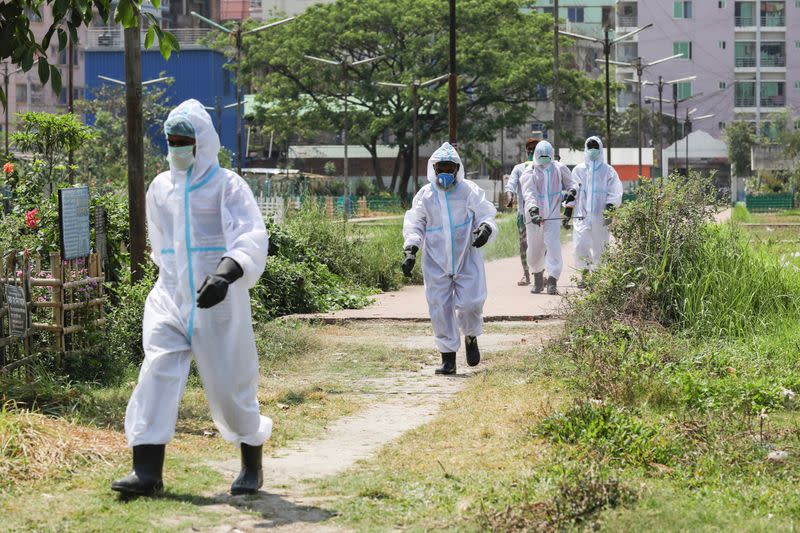 People, wearing protective suits, walk along a graveyard to join in a funeral of a person who died due to coronavirus disease (COVID-19) in Dhaka