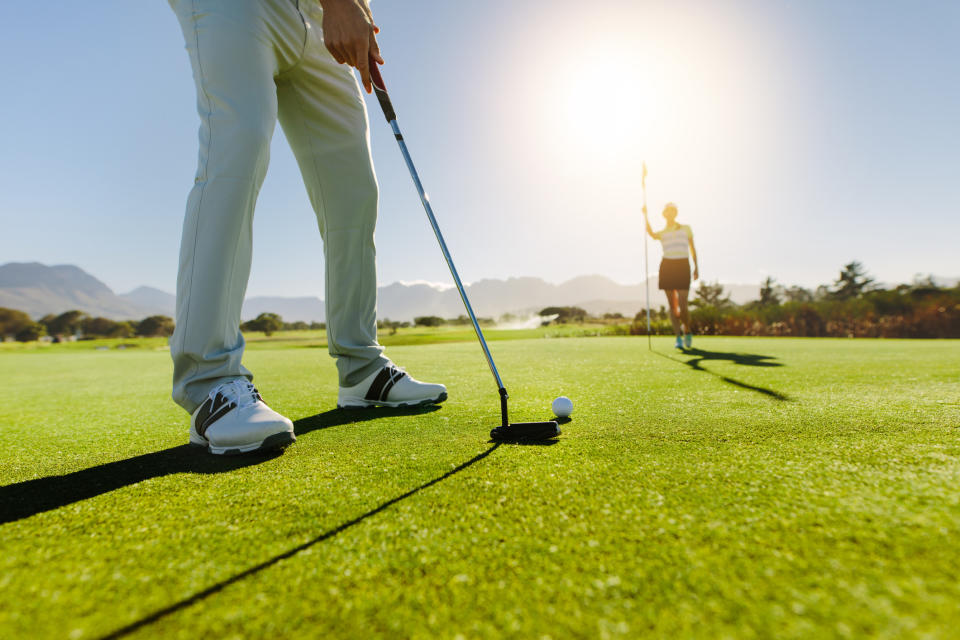 Person playing golf prepares to putt as another stands in distance on green field