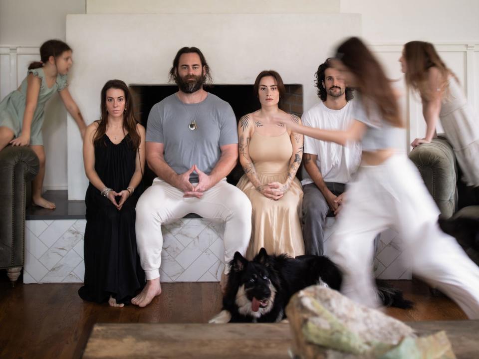 The family sits on by a fireplace as their daughters run around.