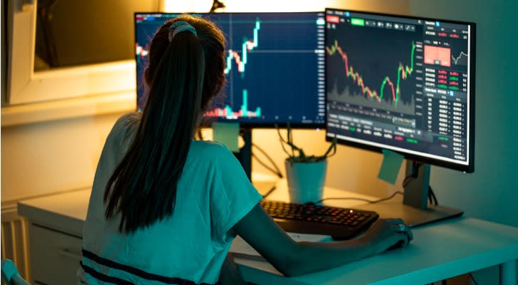 Image shows a trader sitting in front of their computer monitors in order to see the latest stock price information during after-hours trading.