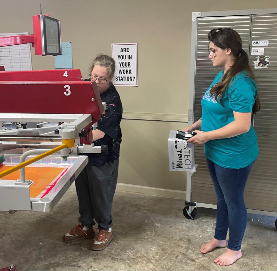 QuesTECH/DayStar general manager Crystal Rhymes showing employee and QuesTECH student Amelia how to properly ink a T-shirt.