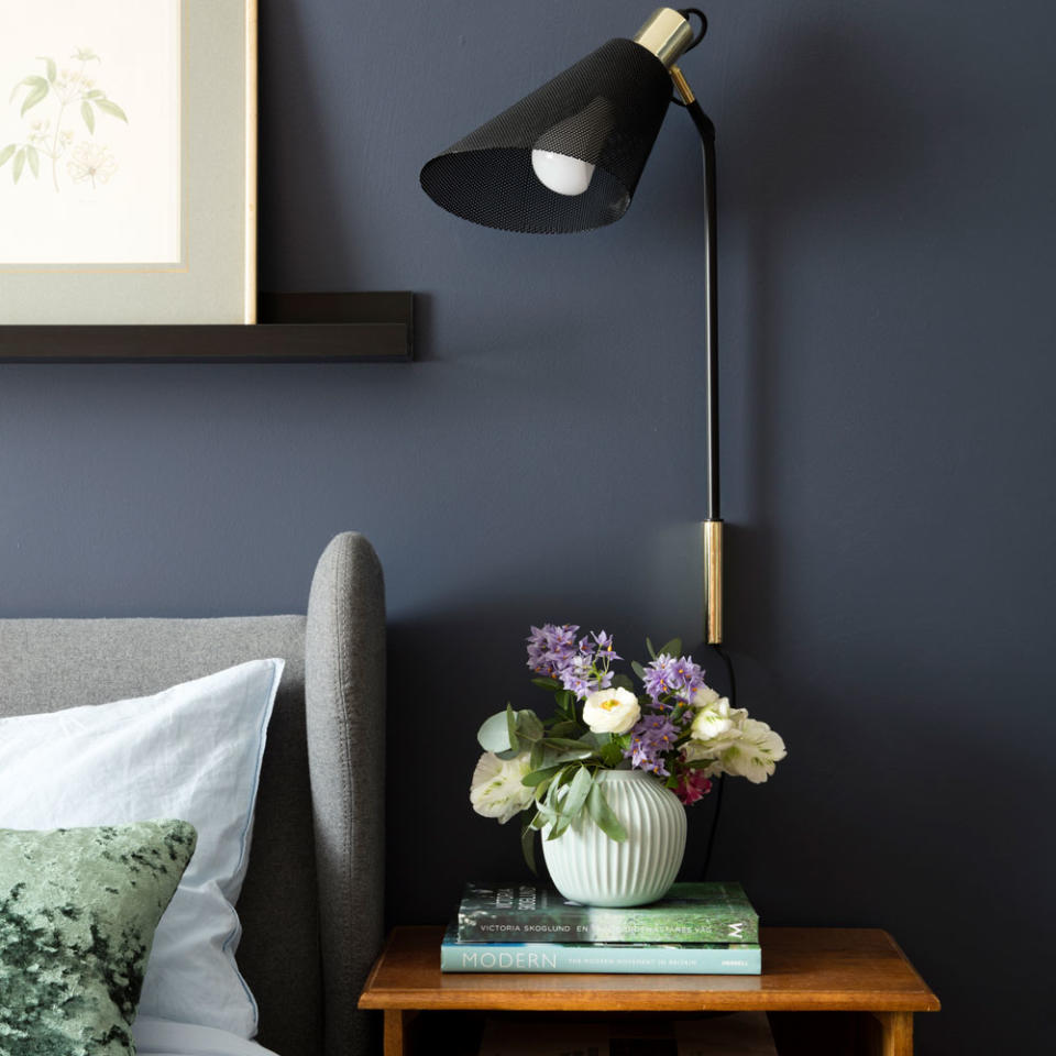 Modern black wall lamp on blue wall above wooden side table.
