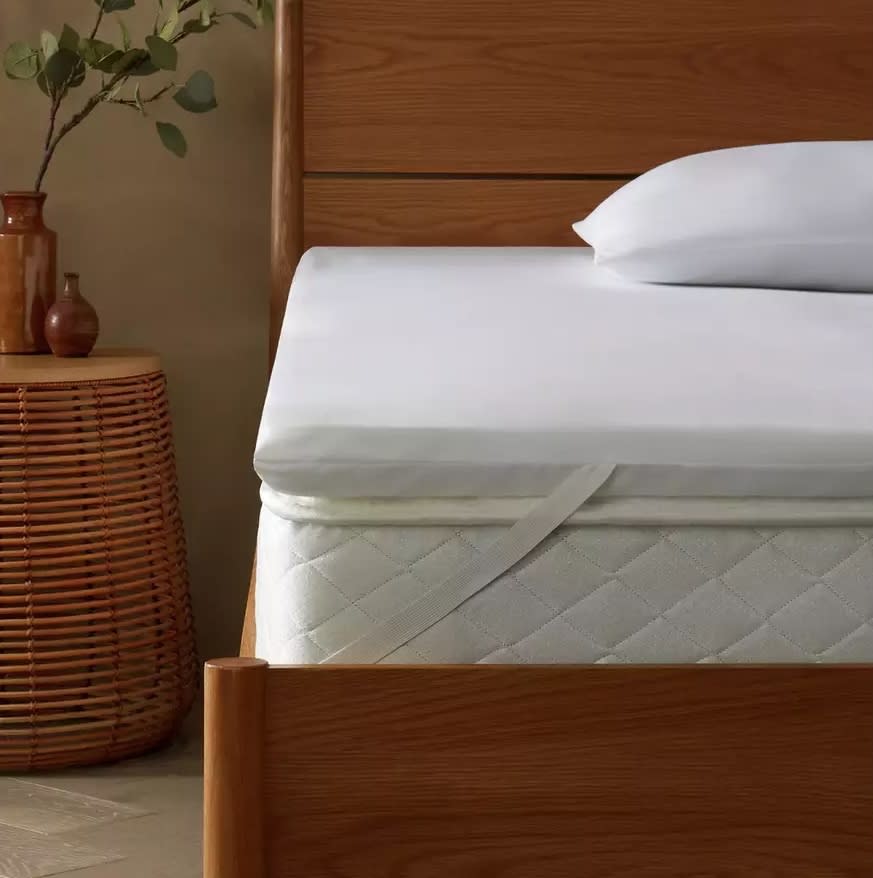 Double bed with a mattress topper with a rattan-style bedside table. 