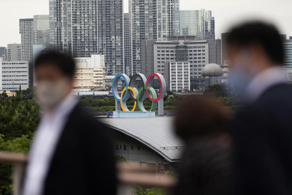 The statue of the Olympics rings overlooks people visiting a nearby shopping mall in Tokyo on Thursday, July 1, 2021. The area is closed off as it's prepared for the postponed Olympics and Paralympics Games planned to start within a month. (AP Photo/Hiro Komae)