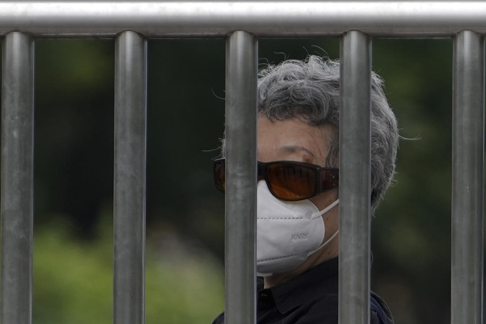 A woman wearing a face mask stands watch behind steel bars on a street in Beijing, Tuesday, June 28, 2022. (AP Photo/Andy Wong)