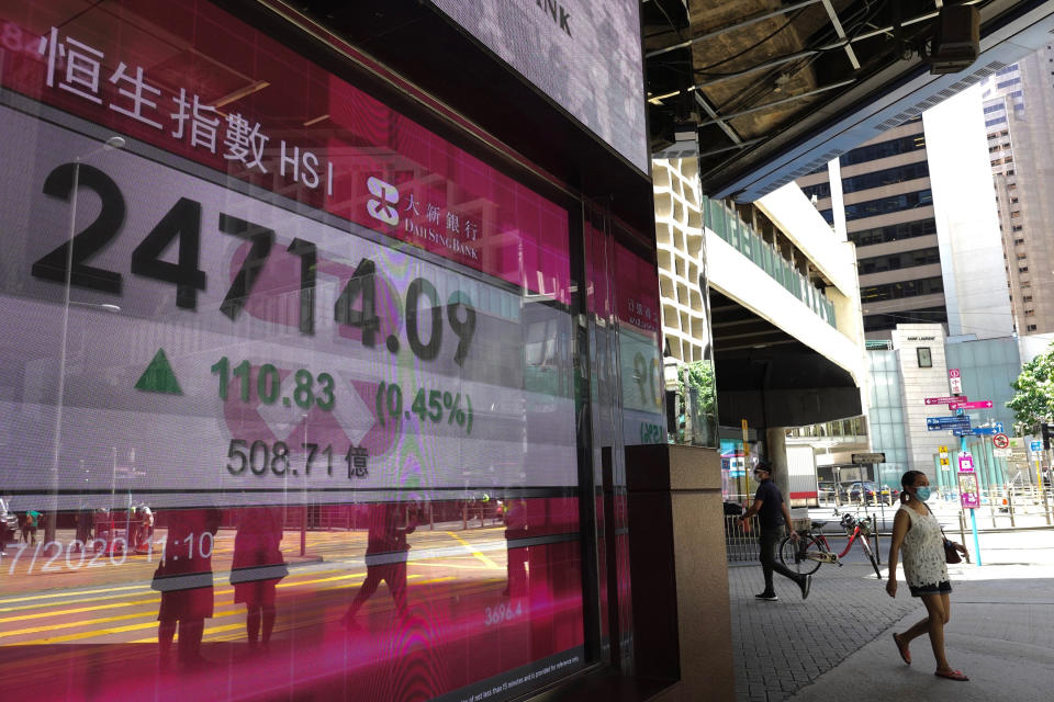 A woman wearing a face mask walks past a bank's electronic board showing the Hong Kong share index at Hong Kong Stock Exchange in Hong Kong Tuesday, July 28, 2020. Shares advanced in Asia on Tuesday after U.S. stocks resumed their upward march on Wall Street, while the price of gold pushed to nearly $1,970 per ounce. (AP Photo/Vincent Yu)