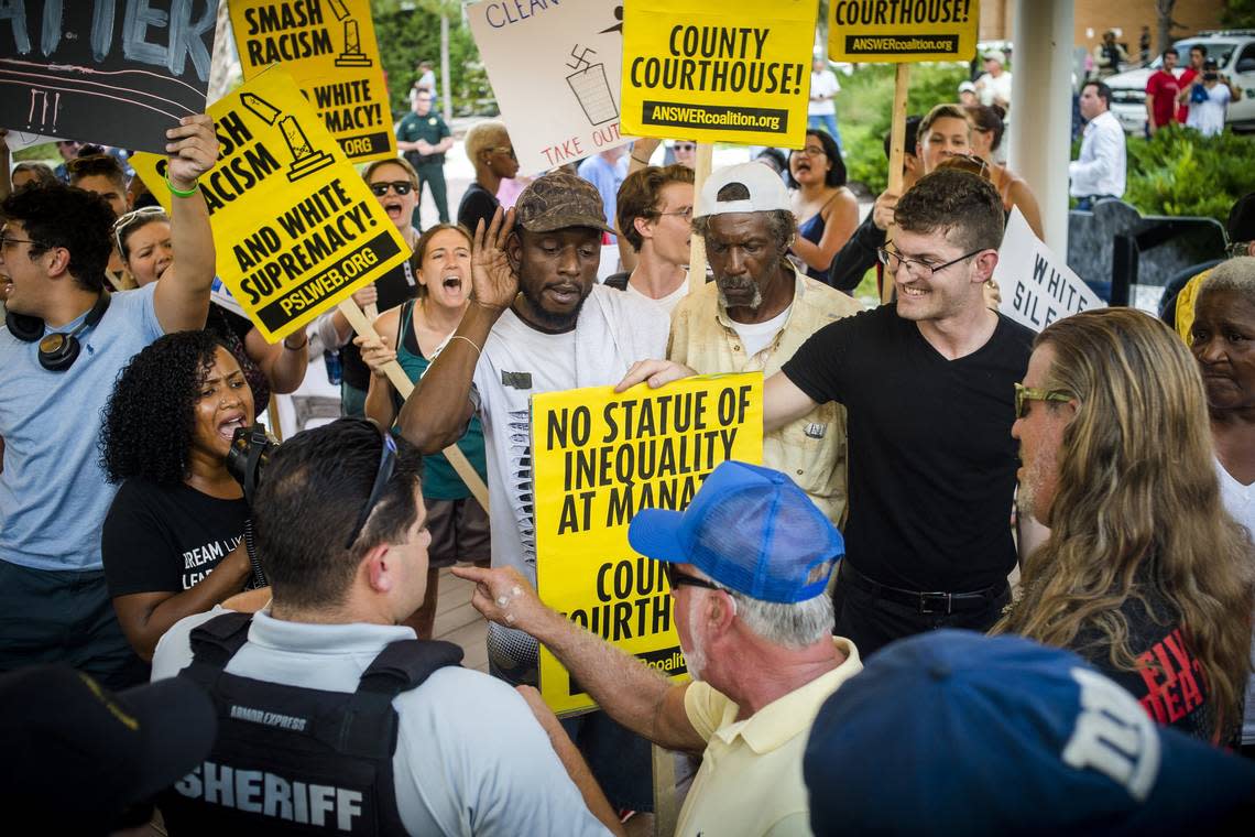 Activists from Black Lives Matter, AntiFa and Answer Coalition hold signs while they argue with pro-monument protestors for the removal of the confederate monument in front of the Manatee County Historic Courthouse on Monday evening in downtown Bradenton.