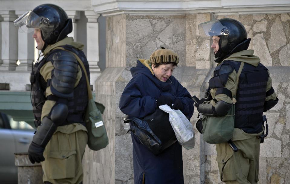 A woman searches for her identity documents standing next to armed men in riot gear, that were performing identity and hand bag checks on people walking near the building of Crimea's regional parliament in Simferopol, Ukraine, Monday, March 17, 2014. Crimea's parliament on Monday declared the region an independent state, after its residents voted overwhelmingly to break off from Ukraine and seek to join Russia. (AP Photo/Vadim Ghirda)