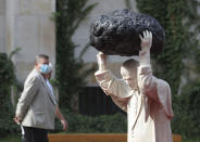 A visitor to the National Museum walks past a new statue of the late pope, St. John Paul II, throwing a stone at a "Poisoned Well" just hours before its official inauguration in the museum yard in Warsaw, Poland, Thursday, Sept. 24, 2020. The sculpture by Poland's Jerzy Kalina is said to be a response to a controversial 1999 sculpture by Italian Maurizio Cattelan in which the Polish-born pontiff was shown as being crushed by a similar stone. (AP Photo/Czarek Sokolowski)