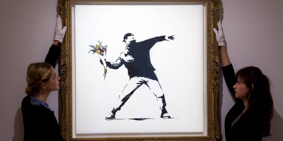 Gallery assistants adjust "Love is in the Air" by British graffiti artist Banksy ahead of its sale at Bonhams auction house in London on June 24, 2013.