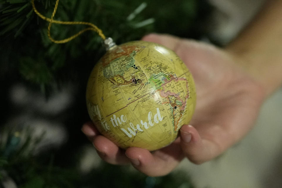 Andy Hazelton holds a globe ornament on which he and his wife have marked the home countries of migrant kids they have fostered, on the family's Christmas tree in Homestead, Fla., Monday, Dec. 18, 2023. Over the last four years, the Hazeltons, a couple in their early 30s with three biological daughters ages 8, 6 and almost 2, have fostered five migrant minors for several months and more for shorter periods. Most came from Central America, but two teen boys were from Afghanistan. (AP Photo/Rebecca Blackwell)