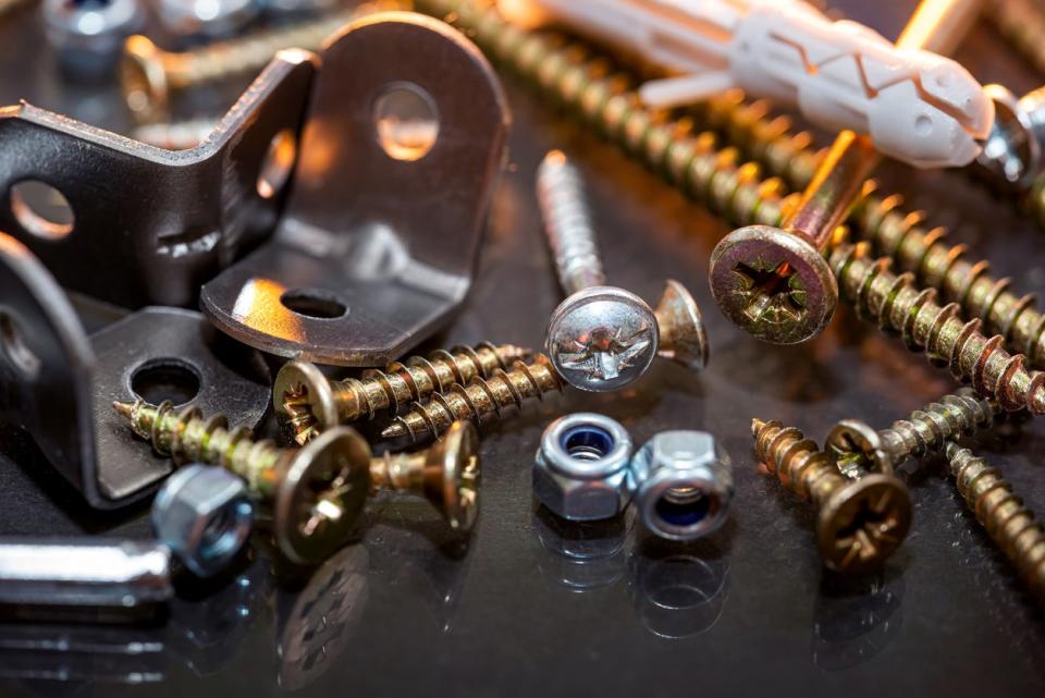 Close-up image of sets of plastic dowels and shiny metal self-tapping screws in a pile on a table background. 