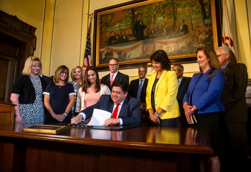 Illinois Gov. J.B. Pritzker, flanked by Bentley Stewart, left, a teacher in the Jacksonville, Ill., School District 117, along with legislators and representatives from the education sector, signs legislation Thursday, Aug. 22, 2019, raising the minimum salary for teachers to $40,000 in the governor's office at the Illinois State Capitol in Springfield, Ill. The new minimum salary will be phased in over four years with hopes to reduce a teacher shortage in Illinois that has school districts for the 2018-19 school year with 4,196 unfilled positions across the state according to the Illinois State Board of Education.