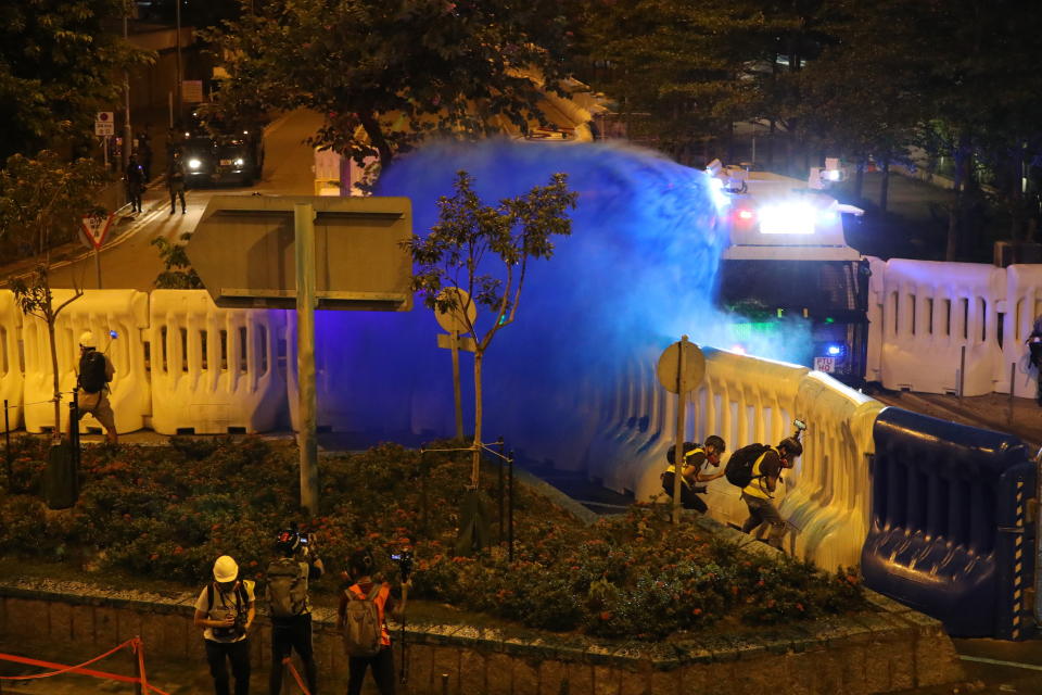Police fire blue-colored liquid on protestors in Hong Kong, Saturday, Sept. 28, 2019. Protesters streamed onto a main road nearby and some targeted government buildings that were barricaded. Police initially used a hose to fire pepper spray after some demonstrators threw bricks. A water cannon truck later fired a blue liquid, used to identify protesters, after protesters lobbed gasoline bombs through the barriers. (AP Photo/Vincent Thian)