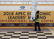 A worker passes by a banner at the APEC 2018 International Media Center at Port Moresby, Papua New Guinea Wednesday, Nov. 14, 2018. After three decades of promoting free trade as a panacea to poverty, the APEC grouping of nations that includes the U.S. and China is holding its lavish annual leaders meeting in the country that can least afford it. (AP Photo/Aaron Favila)