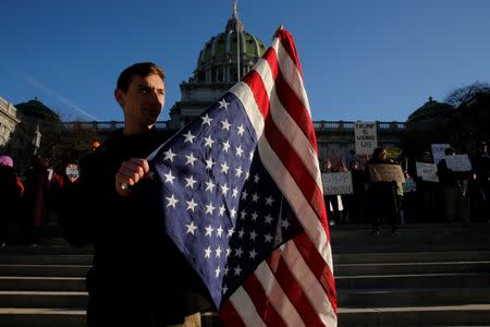 A man holds an upside down flag as people protest against U.S. President-elect Donald Trump as electors gather to cast their votes for U.S. president at the Pennsylvania State Capitol in Harrisburg, Pennsylvania, U.S. December 19, 2016. REUTERS/Jonathan Ernst