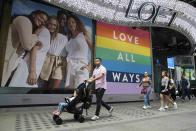 In this Thursday, June 20, 2019, people walk past a pride display at the Loft store in New York's Times Square. For Pride month, retailers across the country are selling goods and services celebrating LGBTQ culture. They range from Macy’s same-sex wedding registries to the Times Square digital billboards beaming apparel sold in shops below. (AP Photo/Mary Altaffer)