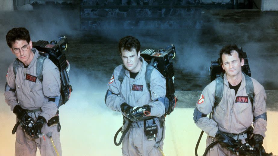 three ghostbusters stand with proton packs at the ready