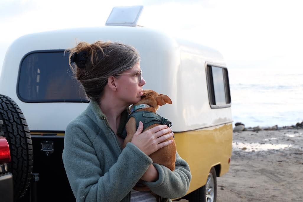 A writer standing in front of her travel trailer with her dog.