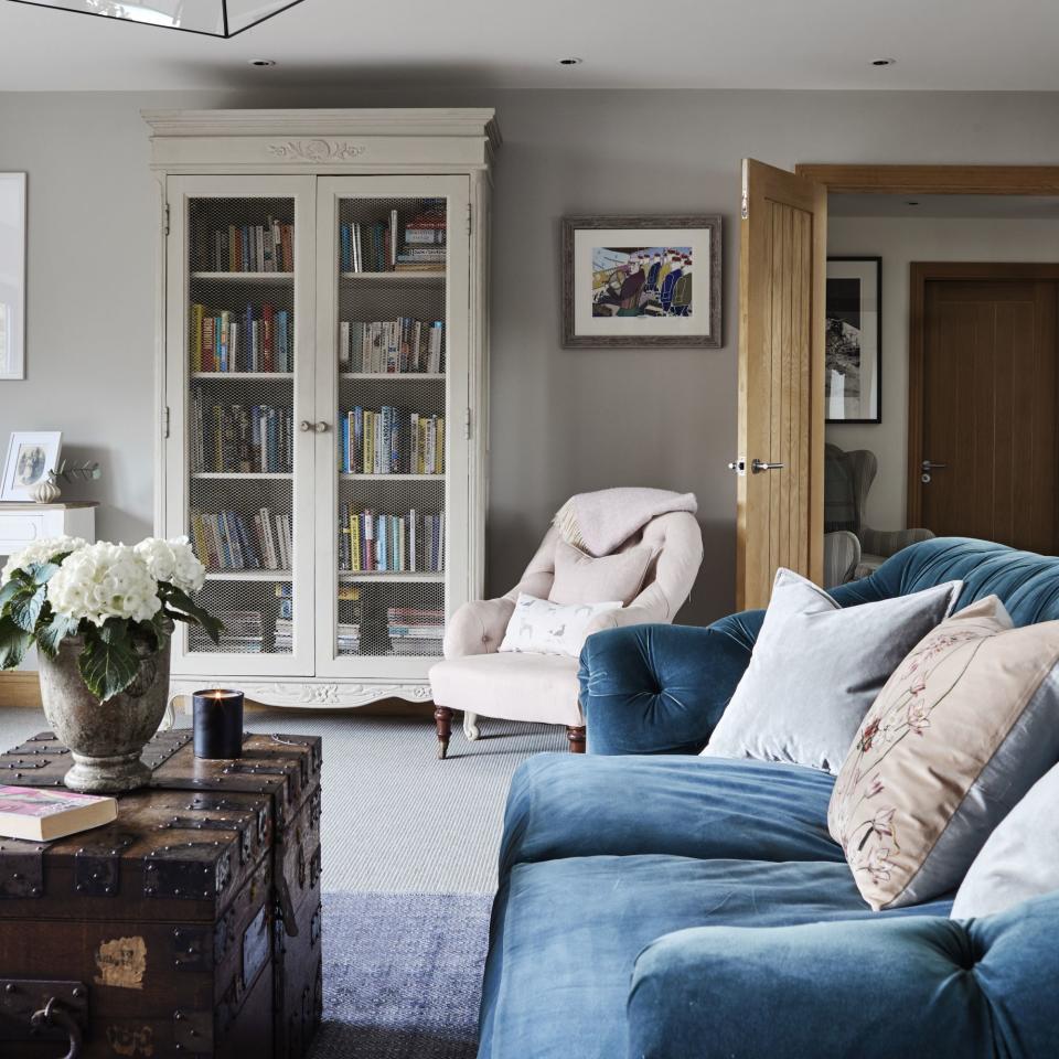 blue sofa with pink and white cushions in living room with coffee table and bookcase