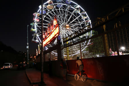 A child climbs on a bike to see an amusement park with an illuminated ferris wheel in Caracas, Venezuela, March 17, 2019. REUTERS/Ivan Alvarado